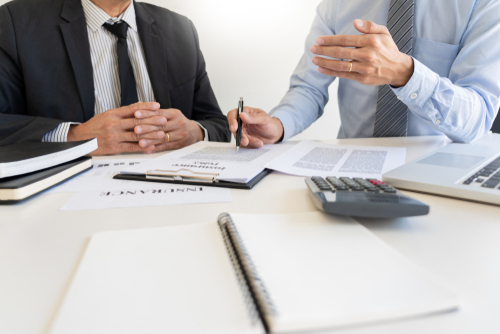 Confident insurance agent broker man holding document and present pointing showing an insurance policy contract form to client Business Communication